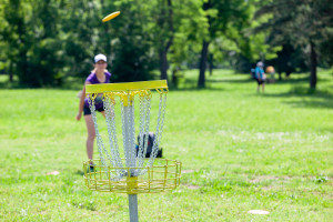 Young woman playing flying disc sport game in the park Disc-Golf-in-North-Central-Massachusetts